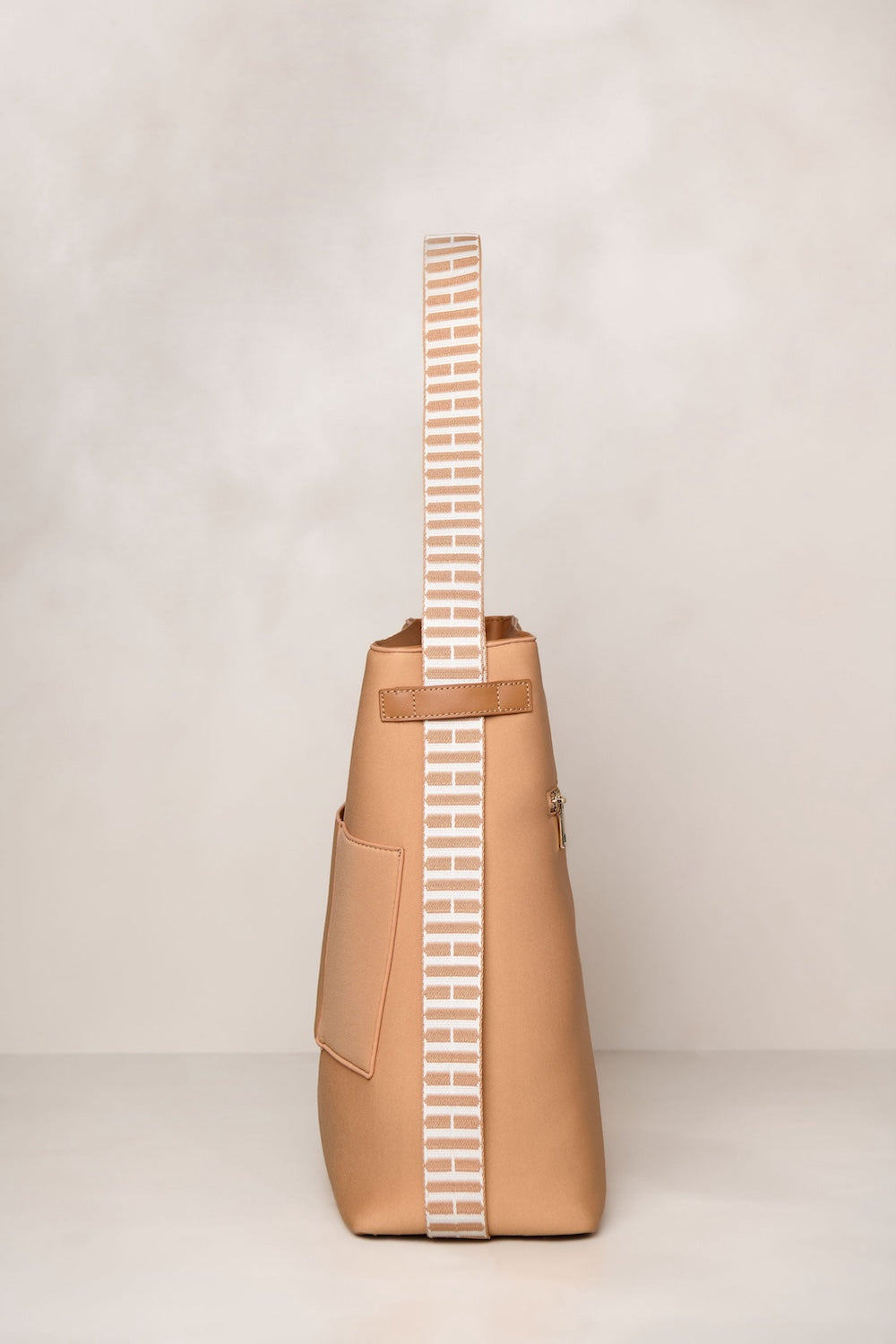 Tan handbag with a striped strap on a light beige background