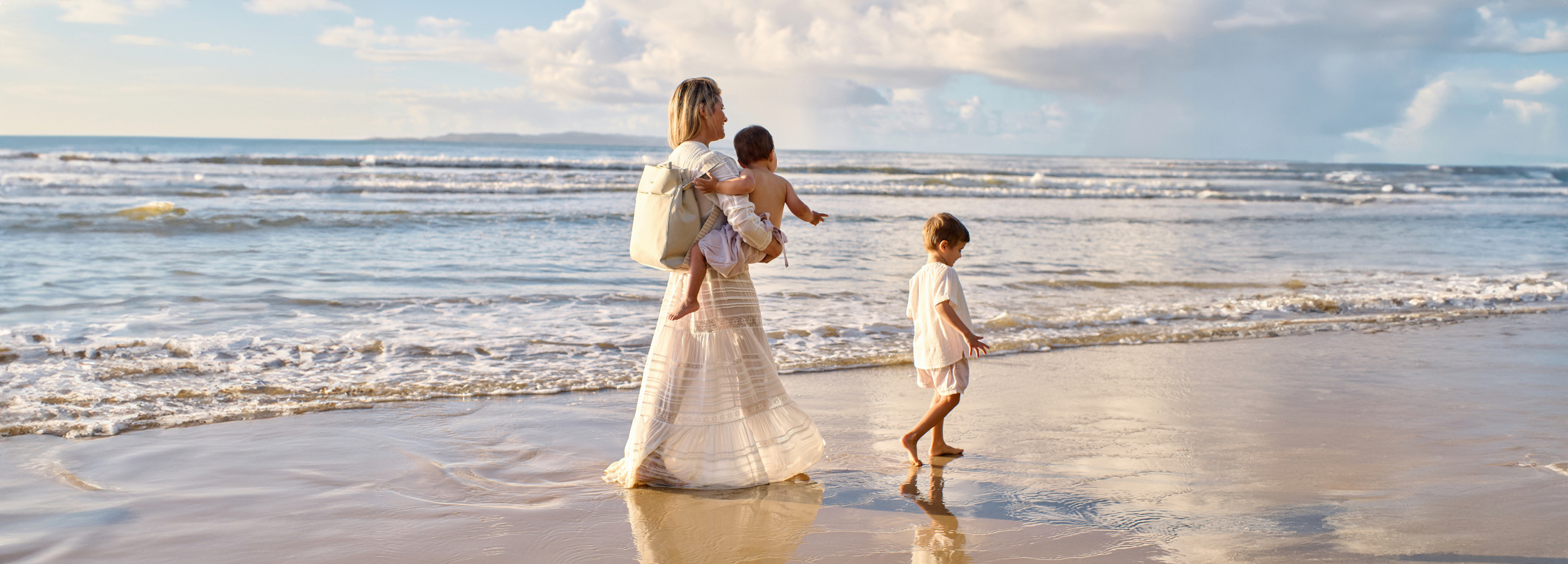 Mum walking on beach with her kids carrying taupe neoprene baby bag as backpack