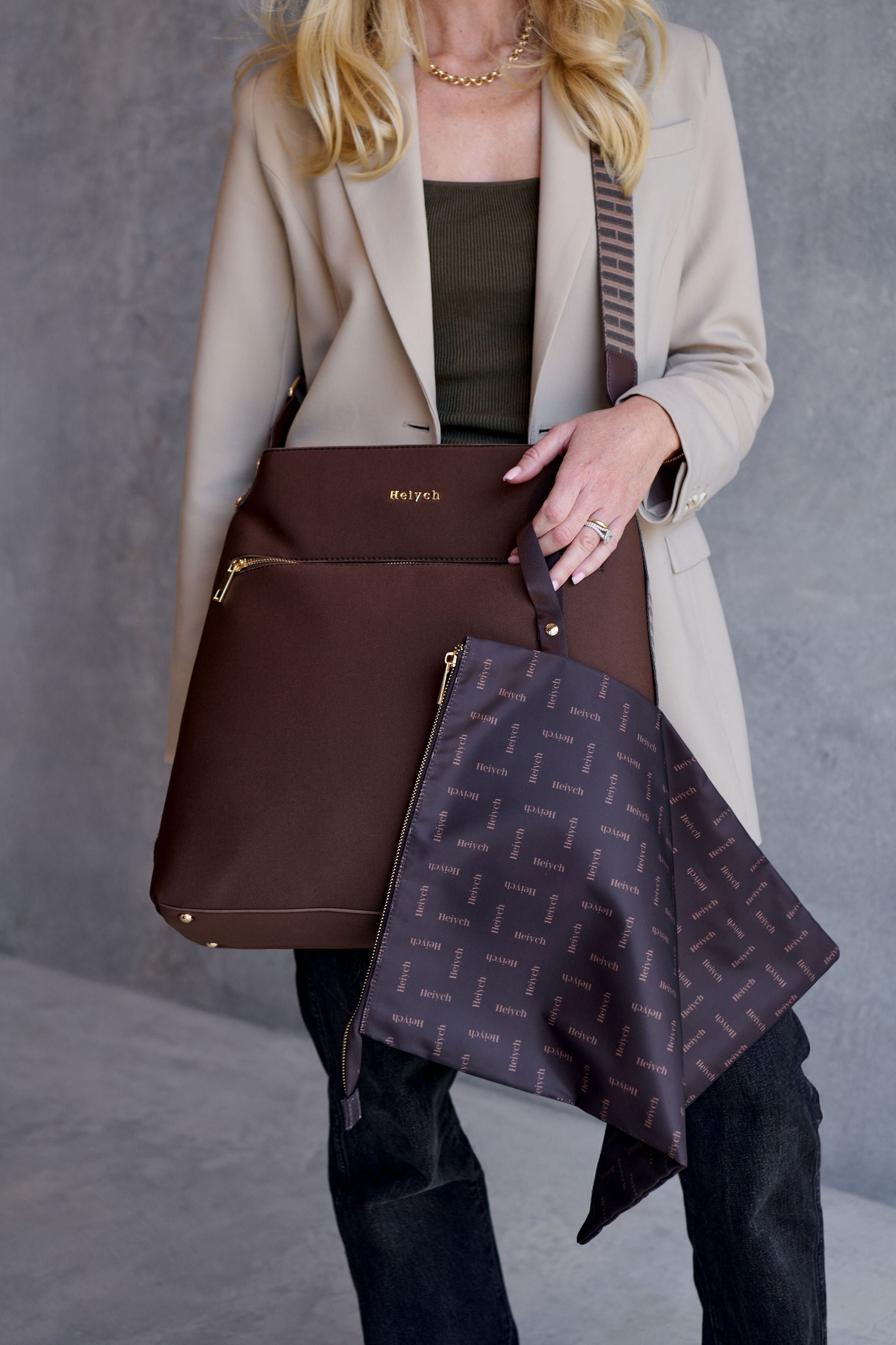 Woman holding a chocolate brown handbag with a matching patterned pouch against a neutral background