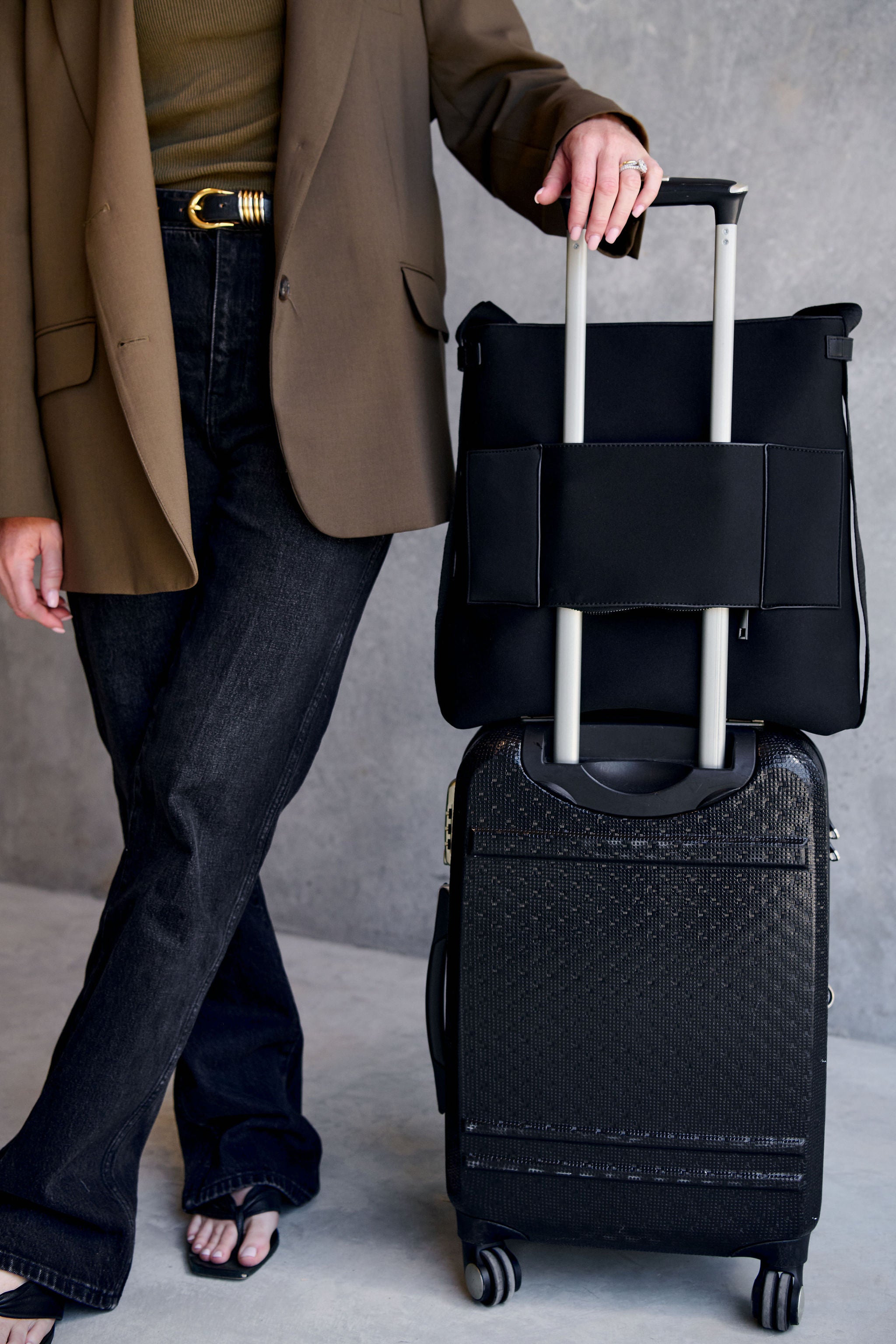 Woman holding a black suitcases against a neutral background with handbag luggage pass through pocket