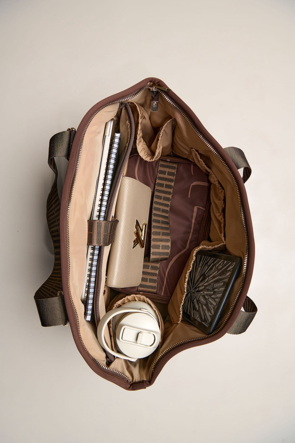 Open brown chocolate bag with various items on a beige background